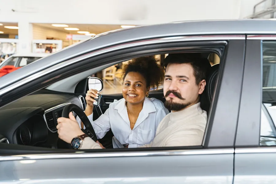 Paar sitzt im neuen Auto und zeigt den Schlüssel